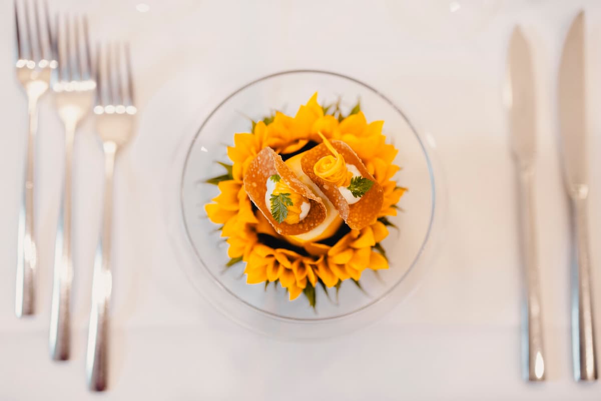 Gehobene Küche: goldene Sonnenblumen-Pasta gekrönt mit knusprigen Tuiles, frischen Kräutern und Zitronenzeste auf weißem Porzellan.